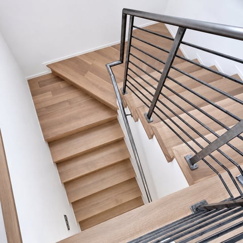 Wooden staircase with metal horizontal cable railing descending between white walls, viewed from above