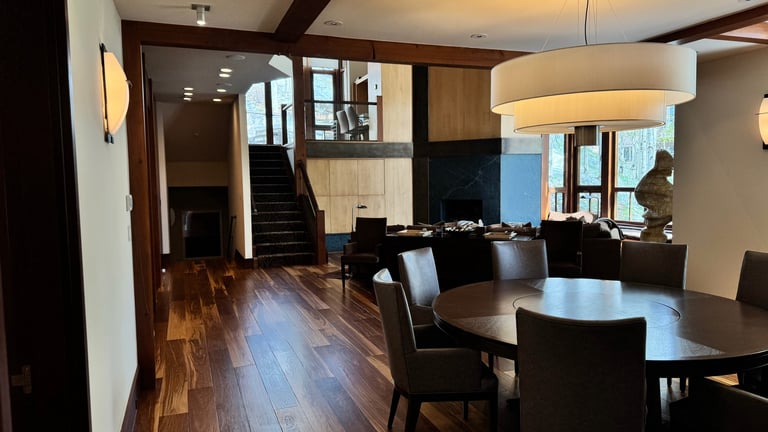 Modern open-concept interior with dark wood flooring, black dining furniture, staircase, and contemporary lighting fixtures.